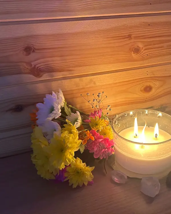 A lit three-wick candle beside a posy of bright flowers and crystals